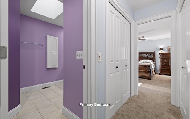 corridor featuring light carpet, a skylight, visible vents, baseboards, and light tile patterned flooring