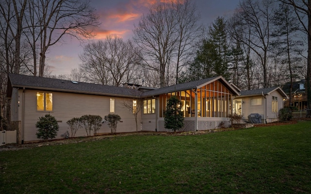 back of property at dusk with a sunroom and a lawn