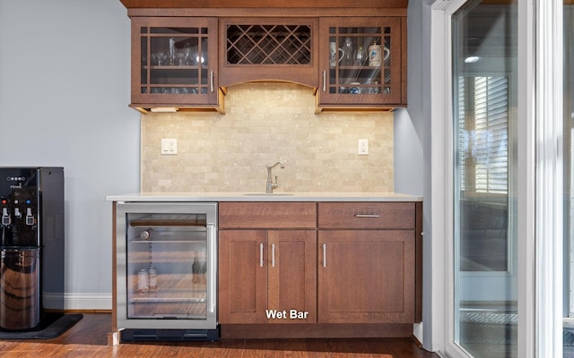 bar with a sink, beverage cooler, baseboards, wet bar, and decorative backsplash