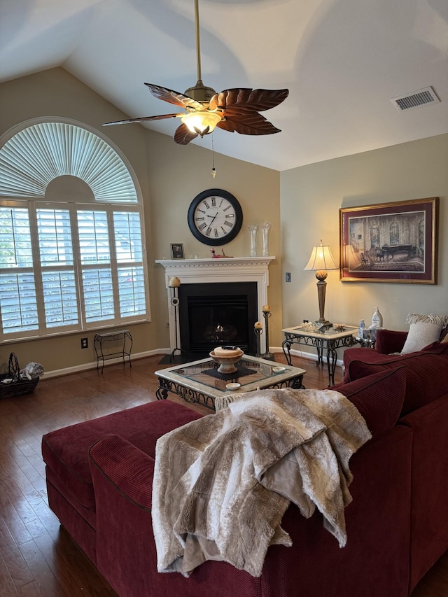 living area with a fireplace with raised hearth, lofted ceiling, dark wood-style flooring, visible vents, and a ceiling fan