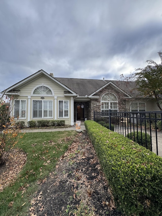 ranch-style home with stone siding, a front lawn, and fence