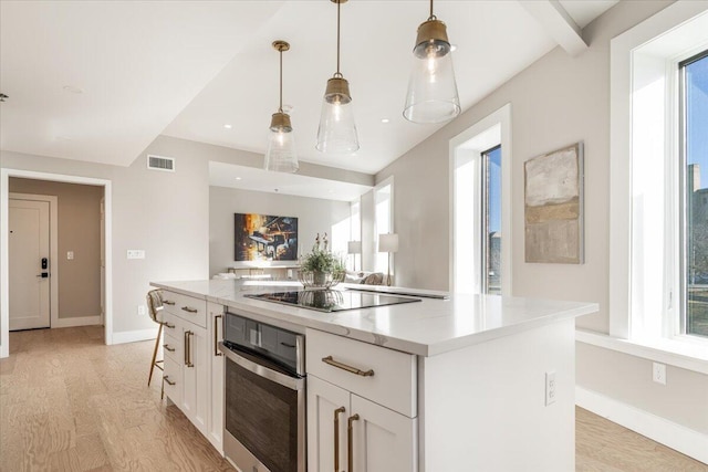 kitchen with oven, a kitchen island, visible vents, white cabinetry, and hanging light fixtures