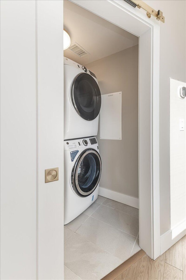 washroom with light tile patterned floors, stacked washer and dryer, laundry area, and baseboards