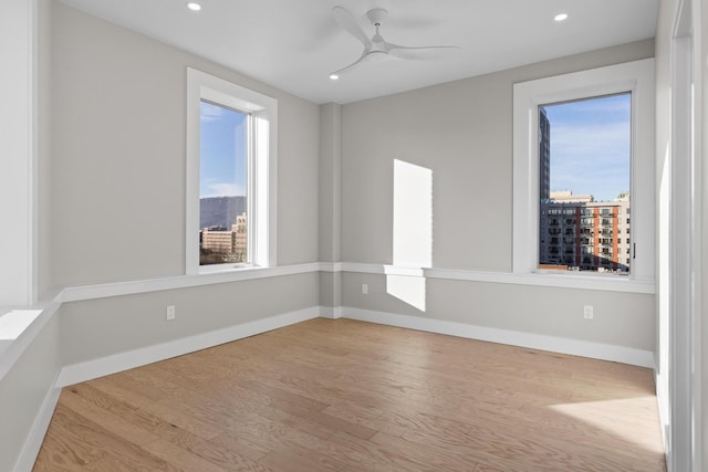 empty room with recessed lighting, a ceiling fan, baseboards, light wood-style floors, and a view of city