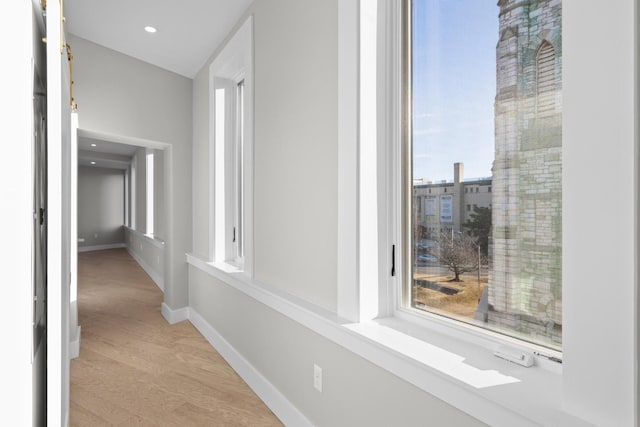 hallway with light wood finished floors, baseboards, a wealth of natural light, and recessed lighting