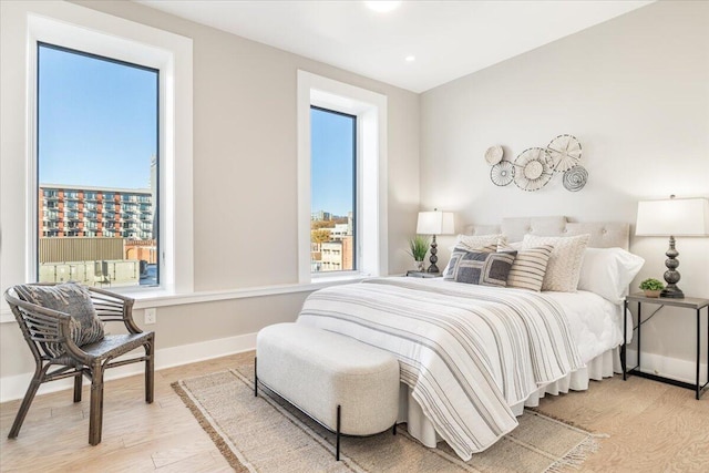 bedroom with light wood-style flooring, a view of city, baseboards, and recessed lighting