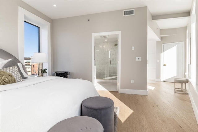 bedroom with light wood finished floors, connected bathroom, visible vents, and baseboards