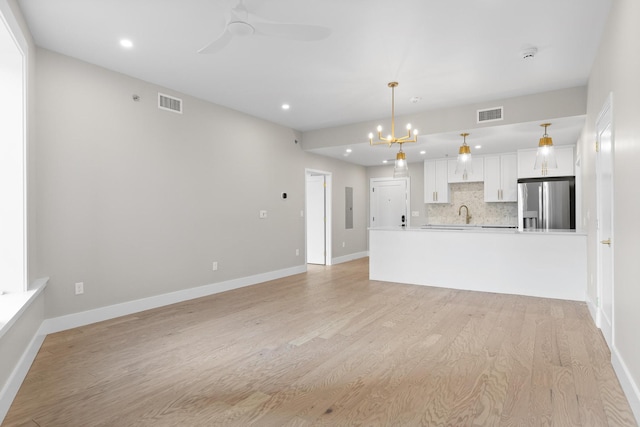 unfurnished living room featuring ceiling fan with notable chandelier, light wood finished floors, visible vents, and electric panel