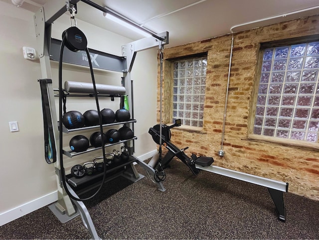 exercise room featuring brick wall and baseboards