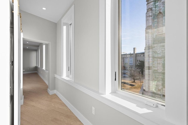 corridor featuring baseboards, a healthy amount of sunlight, light wood finished floors, and recessed lighting