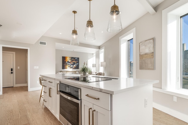 kitchen featuring visible vents, a center island, decorative light fixtures, white cabinets, and oven