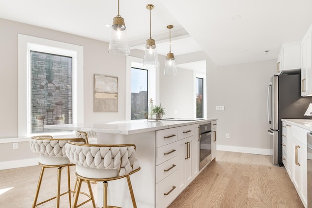 kitchen featuring stainless steel oven, hanging light fixtures, a kitchen bar, and white cabinets