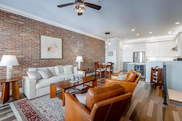 living area featuring beverage cooler, brick wall, wood finished floors, crown molding, and recessed lighting