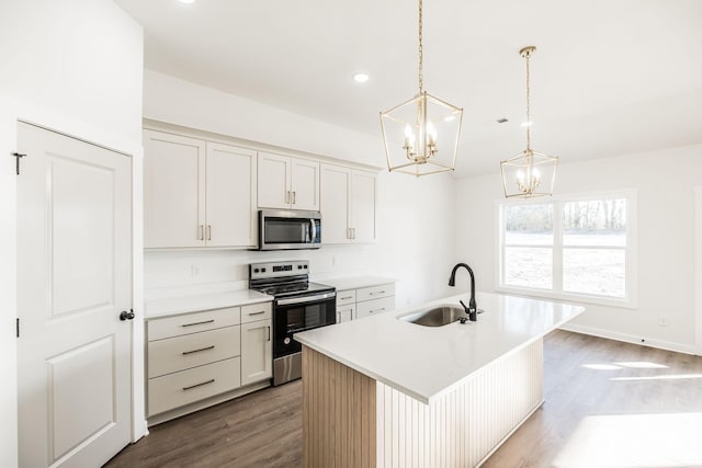 kitchen with a sink, light countertops, appliances with stainless steel finishes, decorative light fixtures, and an island with sink