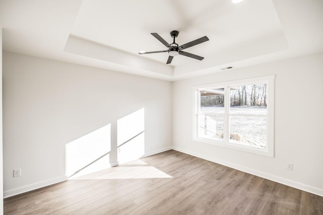 empty room with a raised ceiling, light wood-type flooring, baseboards, and ceiling fan