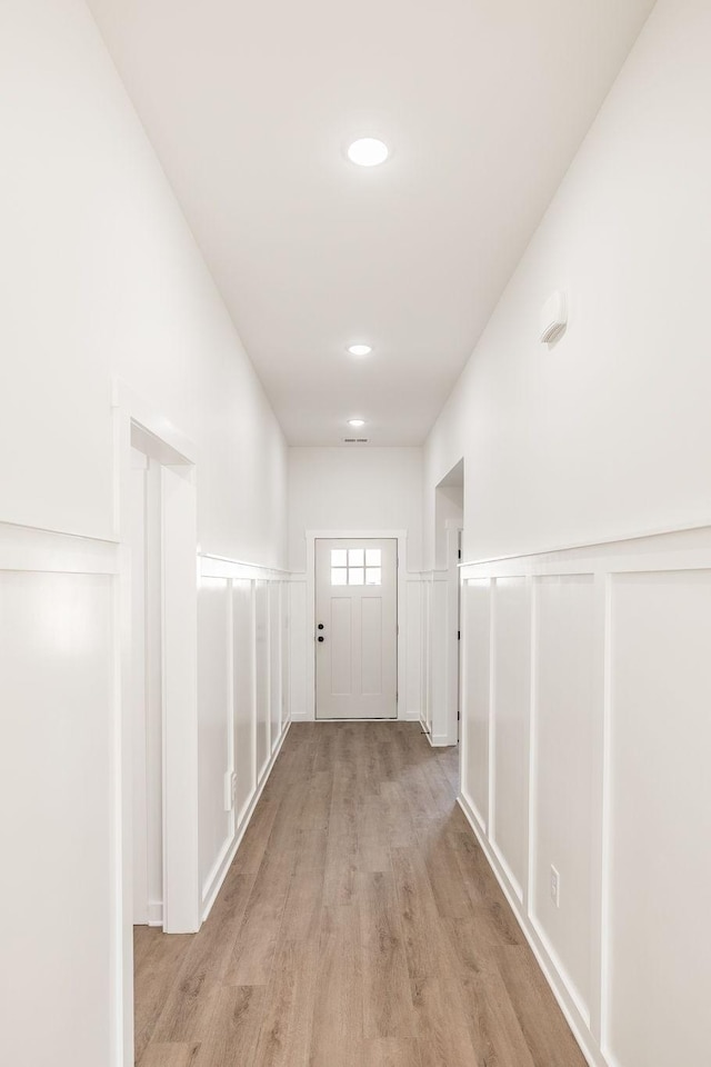 corridor featuring wainscoting, recessed lighting, a decorative wall, and light wood finished floors