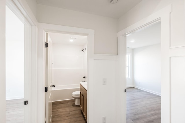 bathroom featuring baseboards, toilet, wood finished floors,  shower combination, and vanity