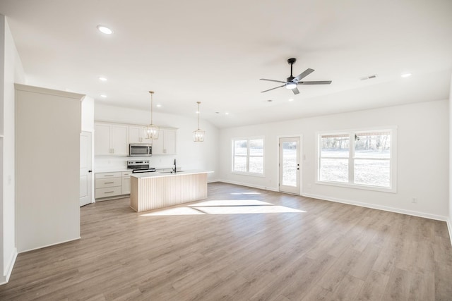 kitchen featuring open floor plan, decorative light fixtures, white cabinets, an island with sink, and stainless steel appliances