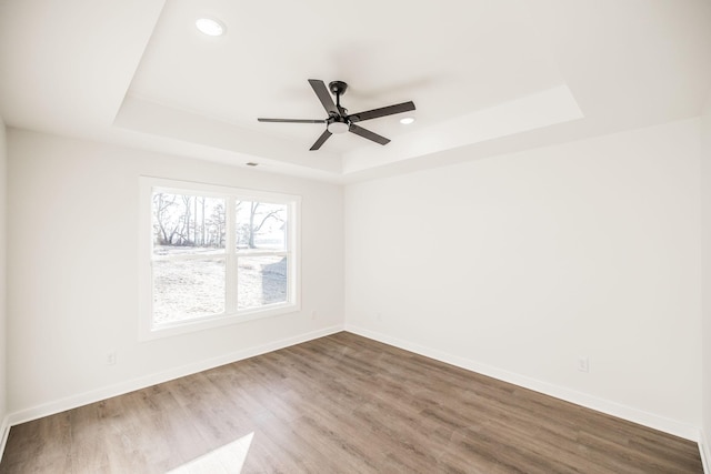 unfurnished room featuring baseboards, a raised ceiling, wood finished floors, and recessed lighting