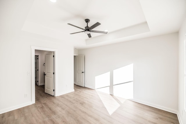 unfurnished room with light wood-style floors, baseboards, a tray ceiling, and a ceiling fan