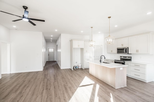 kitchen with decorative light fixtures, a kitchen island with sink, stainless steel appliances, light countertops, and white cabinetry