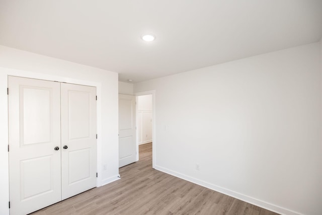 unfurnished bedroom with light wood-style flooring, baseboards, and a closet