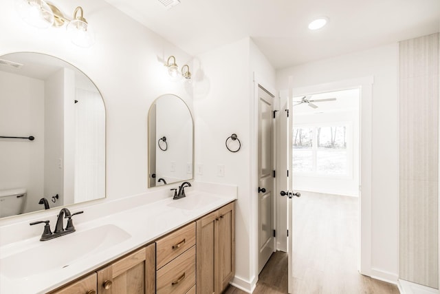 bathroom featuring toilet, double vanity, a sink, and wood finished floors