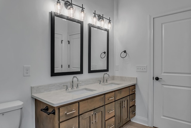 bathroom featuring double vanity, baseboards, toilet, and a sink