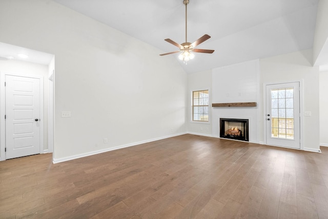 unfurnished living room featuring a wealth of natural light, a warm lit fireplace, lofted ceiling, and wood finished floors