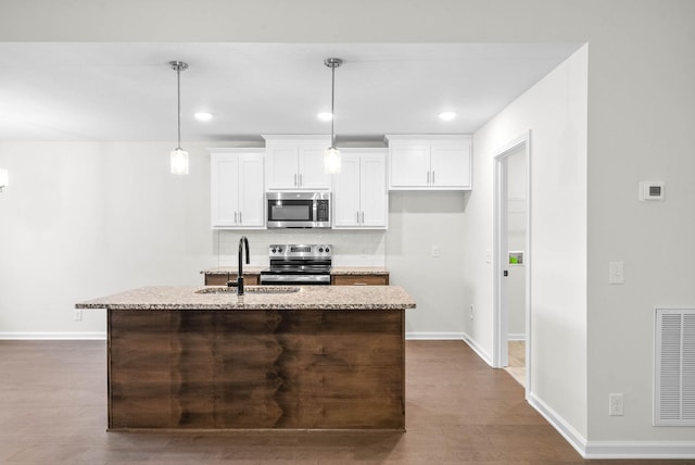 kitchen with a center island with sink, hanging light fixtures, appliances with stainless steel finishes, white cabinetry, and a sink