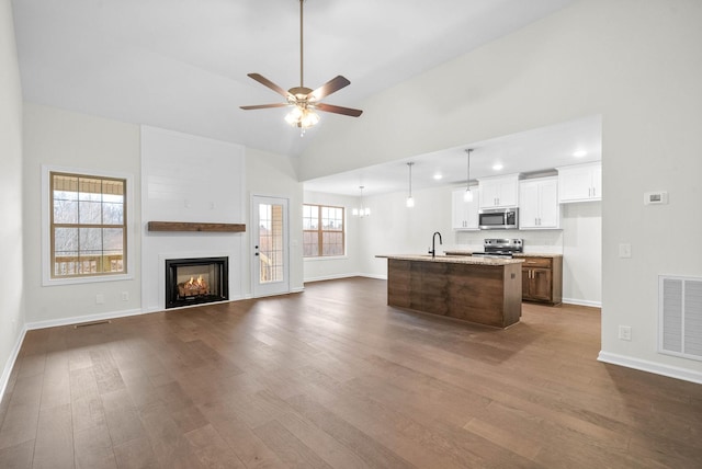 unfurnished living room featuring a warm lit fireplace, visible vents, dark wood finished floors, lofted ceiling, and a sink