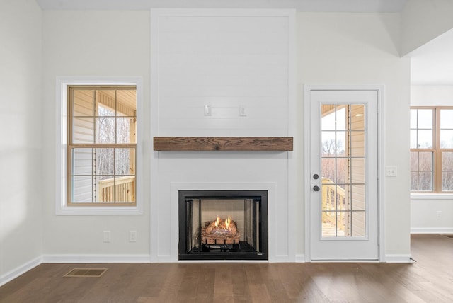 interior space featuring a large fireplace, dark wood-type flooring, visible vents, and baseboards