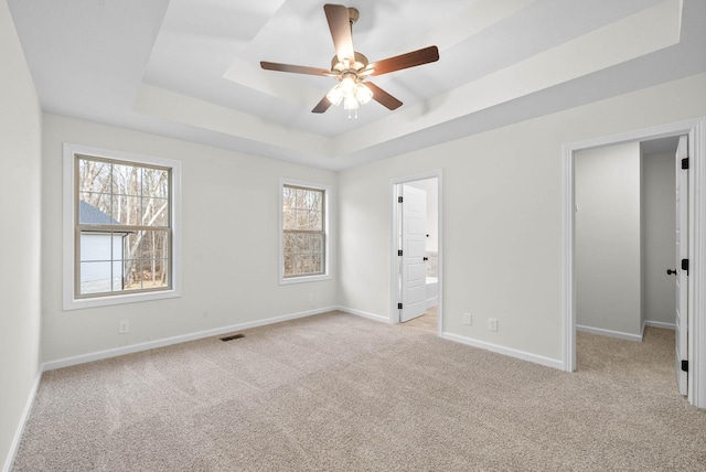 unfurnished bedroom with a spacious closet, a tray ceiling, multiple windows, and baseboards