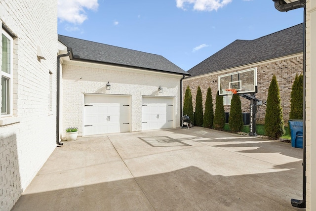 exterior space featuring a garage, roof with shingles, concrete driveway, and brick siding