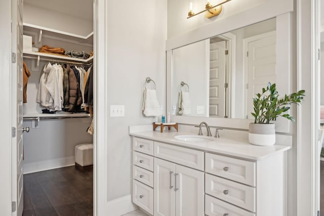 bathroom featuring a spacious closet, baseboards, wood finished floors, and vanity