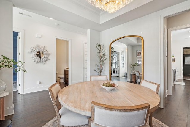 dining room with a notable chandelier, dark wood finished floors, visible vents, a raised ceiling, and crown molding