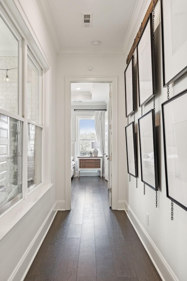 hall with baseboards, dark wood finished floors, visible vents, and crown molding