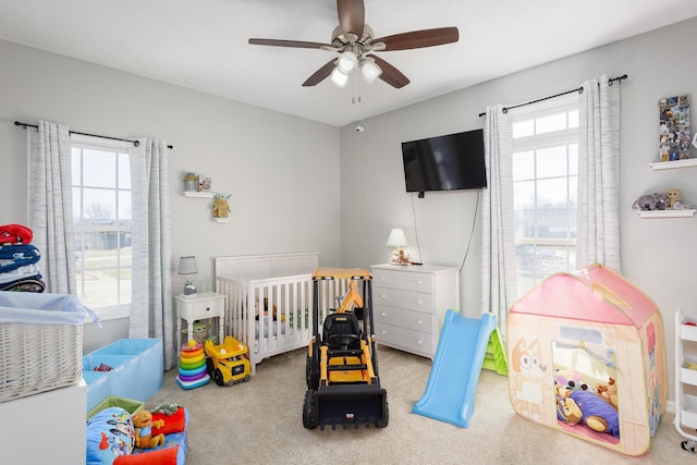 bedroom with light carpet, a nursery area, and a ceiling fan