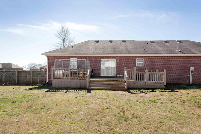 rear view of house featuring brick siding, a yard, a shingled roof, fence, and a deck