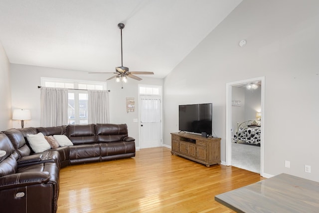 living room featuring ceiling fan, high vaulted ceiling, light wood-style flooring, and baseboards