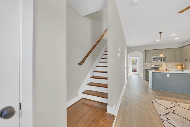 stairway with arched walkways, recessed lighting, wood finished floors, and baseboards