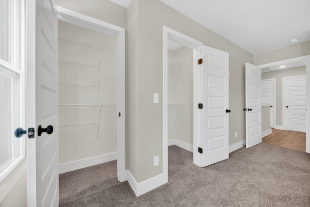 unfurnished bedroom featuring baseboards, a walk in closet, a closet, and light colored carpet