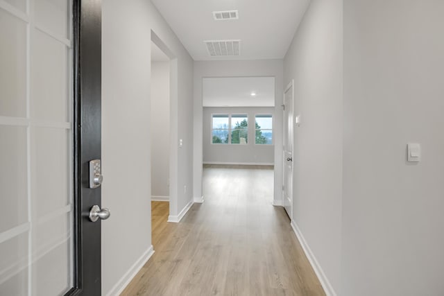 hallway with light wood finished floors, baseboards, and visible vents