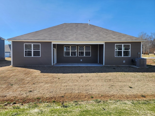 rear view of house with a patio area, central AC unit, a lawn, and roof with shingles