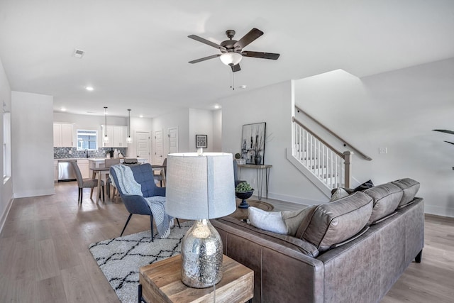 living room with light wood-style floors, visible vents, stairs, and a ceiling fan