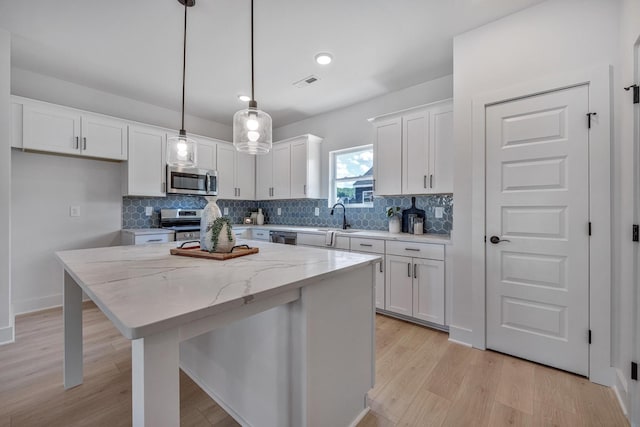 kitchen featuring hanging light fixtures, white cabinetry, stainless steel appliances, and a center island