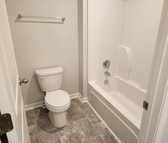 full bath featuring shower / washtub combination, stone finish floor, toilet, and baseboards