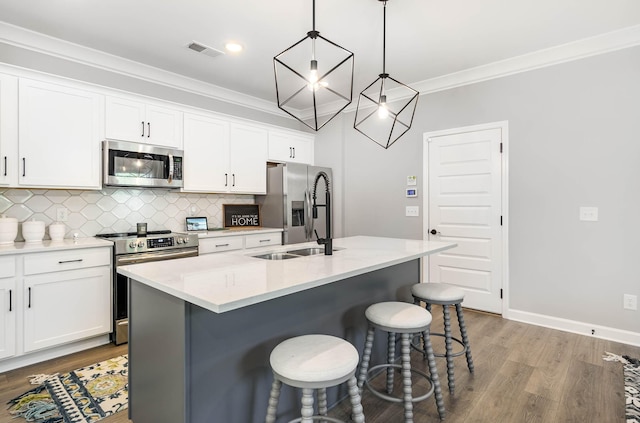 kitchen with decorative light fixtures, a center island with sink, light countertops, appliances with stainless steel finishes, and white cabinetry