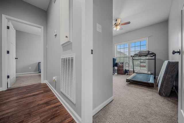 hall featuring dark colored carpet, dark wood-style flooring, visible vents, and baseboards