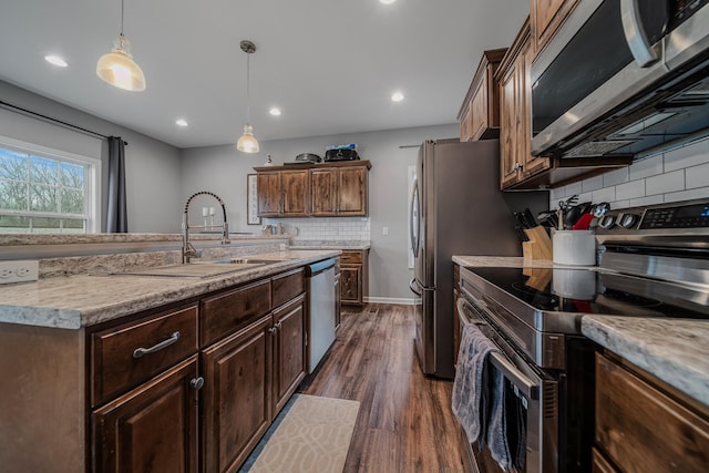 kitchen with dark wood-style flooring, stainless steel appliances, tasteful backsplash, hanging light fixtures, and a sink